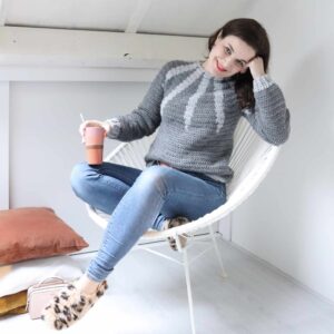 Vrouw in een zelfgehaakte grijze trui met een kop koffie