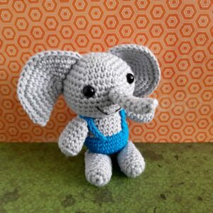 Gehaakte grijze olifant met blauw shirtje tegen een oranje achtergrond
